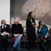 Four people sitting in front of a very large picture of a brain hanging on the wall