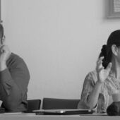 Schwarz-weiß Fotografie von Isabel Wünsche und Bojan Jović. Die beiden sitzen an einem Konferenztisch.