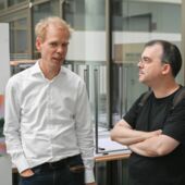 Matthias Schwartz und Henning Trüper stehen im Atrium des Institus für Kulturwissenschaft der HU Berlin und unterhalten sich.