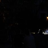Tabea Hertzog and Cord Riechelmann sit outside at a table lit by small lanterns. It is dark around them and you can make out the outlines of the audience.
