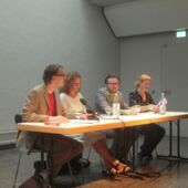 Die vier Autor*innen sitzen auf einem Podium. Falko Schmieder spricht ins Publikum.