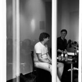 Schwarz-Weiß-Fotografie von Steffen Popp und Jakob Gehlen, aufgenommen durch ein halboffenes Fenster. Die beiden sitzen im Gespräch vor einer Publikumsmenge.