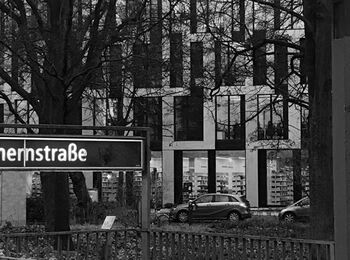 Black and white image of the Spichernstraße subway station entrance on the side of Gerhardt-Hauptmann-Anlage. The new ACHTUNDEINS building can be seen in the background, with cars parked in front of it.