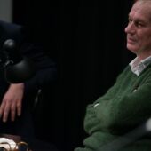 Close-up of Josef Winkler speaking into a microphone, Daniel Weidner sitting next to him