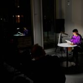 Anja Kümmel sits at a small round table, illuminated by a desk lamp, and reads from a book.