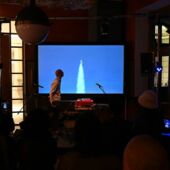 Der Musiker Adi Gelbart blickt während seines Auftritts auf die hinter ihm angebrachte Leinwand, die den Start einer Rakete zeigt.