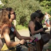 Mehrere Personen stehen an einem Weg im Volkspark Hasenheide und hören über Headset der Führung von Cord Riechelmann zu. Die Person im Vordergrund stützt sich auf ihr Fahrrad.