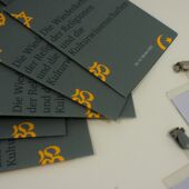 Close-up of some brochures for the annual conference labeled with the conference‘s title in German with some name tags next to them.