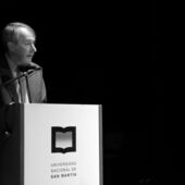 Black and white photo of a speaker during the ceremony, at a lectern with the logo of the university