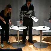 Johanne Mohs, Pola Groß, Jona Spreter and Ivana Sokola move around two tables with microphones on them. They hold printed paper in their hands and smile at each other.