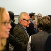 Aage Hansen-Löve stands among the crowd, Susi K. Frank blurred in the foreground