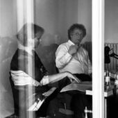 Black and white photograph of Ulrike Vedder and Ingo Schulze, taken through a window. Both gesture and seem to be thoughtful.