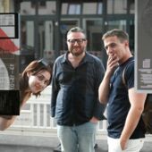 Salome Rodeck, Zaal Andronikashvili und Oliver Precht stehen auf der Straße und schauen durchs Fenster in den Seminarraum. Alle drei lächeln.