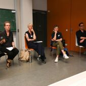 Katrin Trüstedt, Birgit M. Kaiser, Kathrin Thiele, and Daniel Loick sit in a semicircle in front of a green board in the lecture hall and are looking towards the audience..