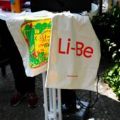 Auf einem weißen Stehtisch liegen zwei Jutebeutel. Einer trägt in rot die Aufschrift »Li-Be«, der andere zeigt ein bunt gestaltetes Einmachglas mit dem Schriftzug »Li-Be. Literaturhaus Berlin«.