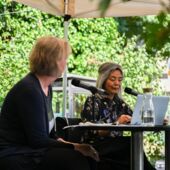 Ulrike Vedder und Yoko Tawada sitzen auf einer Bühne und sprechen miteinander. Vor Tawada steht ein silberner Laptop.