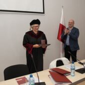 Sigrid Weigel im Talar hält ihre Urkunde und Medaille in den Händen, neben ihr steht Giga Zedania und applaudiert