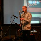 Der Musiker Adi Gelbart spielt Saxophon auf einer Bühne.