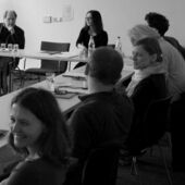 Schwarz-weiß Fotografie von Konferenzteilnehmer*innen am Konferenztisch.