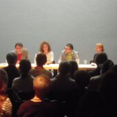 Die vier Autor*innen sitzen auf einem Podium. Falko Schmieder spricht ins Publikum.