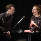 Johannes Becker listens to Judith Keller while she speaks into a microphone