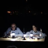 Tabe Hertzog and Cord Riechelmann are sitting at a table illuminated by desk lamps in front of microphones. It is dark around them.